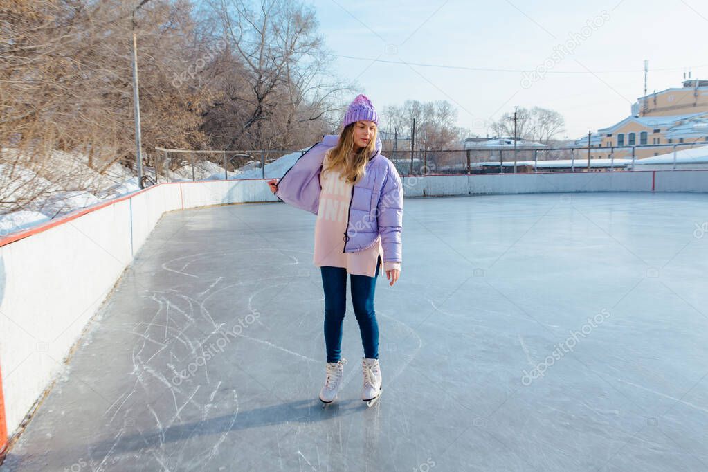 Lovely young woman with riding ice skates on the ice rink.