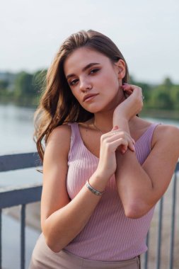 Gün batımında nehrin üzerindeki eski paslı nakliye köprüsünde poz veren genç ve güzel bir kadının ılık yaz portresini kapatın..