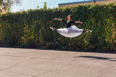 Beyaz etekli kadın balerin altın bir sonbahar parkında sivri ayakkabılarla dans ediyor. Balerin atlayışı yapıyor.