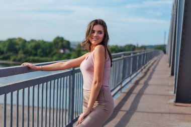 Gün batımında nehrin üzerindeki eski paslı nakliye köprüsünde poz veren genç ve güzel bir kadının ılık yaz portresi..