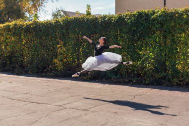 Beyaz etekli kadın balerin altın bir sonbahar parkında sivri ayakkabılarla dans ediyor. Balerin atlayışı yapıyor.