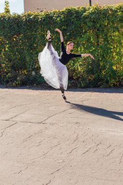 Beyaz etekli kadın balerin altın bir sonbahar parkında sivri ayakkabılarla dans ediyor. Balerin güzel bir bale pozisyonunda duruyor.