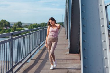 Gün batımında nehrin üzerindeki eski paslı nakliye köprüsünde poz veren genç ve güzel bir kadının ılık yaz portresi..