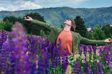 Yeşil ceketli uzun boylu yakışıklı bir adam lupin çiçeği tarlasında duruyor, doğanın güzelliğini emrediyor. Mor ve pembe lupinlerle çevrili bir adam..