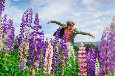 Yeşil ceketli uzun boylu yakışıklı bir adam lupin çiçeği tarlasında duruyor, doğanın güzelliğini emrediyor. Mor ve pembe lupinlerle çevrili bir adam..