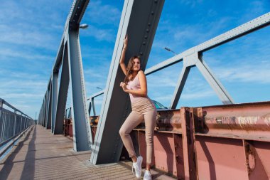 Gün batımında nehrin üzerindeki eski paslı nakliye köprüsünde poz veren genç ve güzel bir kadının ılık yaz portresi..