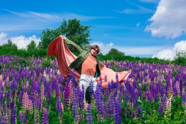 Yeşil ceketli uzun boylu yakışıklı bir adam lupin çiçekleri tarlasında duruyor pembe bir bezle, doğanın güzelliğini emrediyor. Mor ve pembe lupinlerle çevrili bir adam..