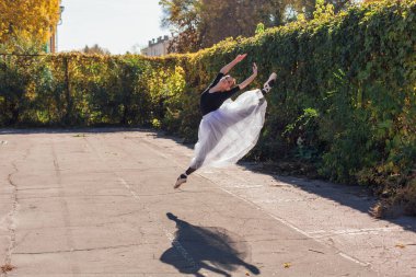 Beyaz etekli kadın balerin altın bir sonbahar parkında sivri ayakkabılarla dans ediyor. Balerin atlayışı yapıyor.