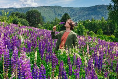 Yeşil ceketli uzun boylu yakışıklı bir adam lupin çiçeği tarlasında duruyor, doğanın güzelliğini emrediyor. Mor ve pembe lupinlerle çevrili bir adam..
