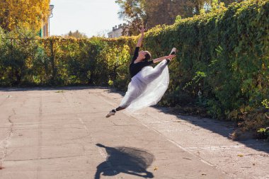 Beyaz etekli kadın balerin altın bir sonbahar parkında sivri ayakkabılarla dans ediyor. Balerin atlayışı yapıyor.