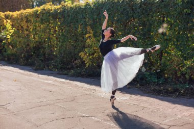 Sonbahar parkında beyaz etekli kadın balerin sivri uçlu ayakkabılarla dans ediyor..