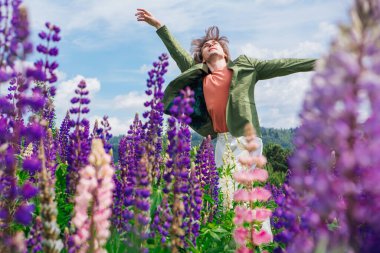 Yeşil ceketli uzun boylu yakışıklı bir adam lupin çiçeği tarlasında duruyor, doğanın güzelliğini emrediyor. Mor ve pembe lupinlerle çevrili bir adam..