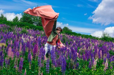 Yeşil ceketli uzun boylu yakışıklı bir adam lupin çiçekleri tarlasında duruyor pembe bir bezle, doğanın güzelliğini emrediyor. Mor ve pembe lupinlerle çevrili bir adam..