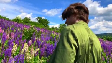 Lupin çiçeklerinin üzerinde duran uzun boylu yakışıklı adam tarlaya döner ve gülümser.