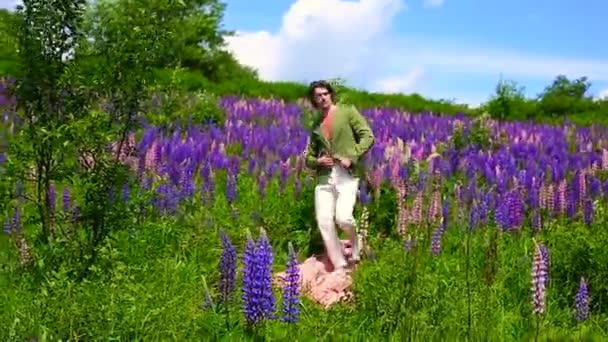 Wysoki przystojny mężczyzna chodzenie na różowy materiał w łubin kwiaty pole — Wideo stockowe