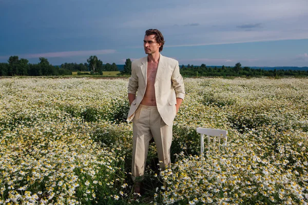 背の高いハンサムな男服を着て上の白いスーツ上の裸体立って上のカモミールの花のフィールド — ストック写真