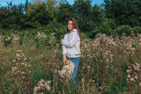 stock image Beautiful brunette teenage girl dressed in a white sweater, jeans and cowboy straw hat standing in dry brown bur grass, smiling and laughing during sunset