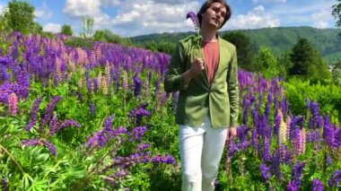 Uzun boylu yakışıklı bir adam lupin çiçekli bir tarlada duruyor.