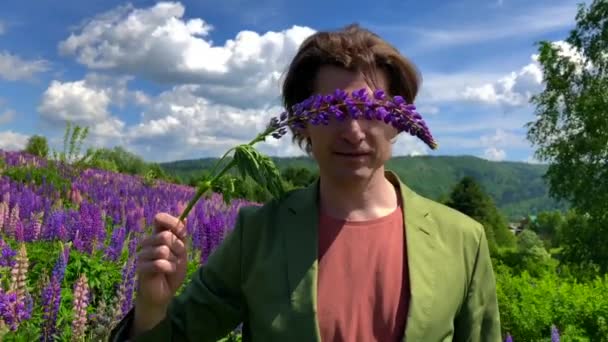 Tall handsome man standing on lupine flowers field with eyes closed by a flower of lupine — Stock Video