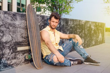 Sakallı, genç ve yakışıklı bir adam sokakta uzun tahtayla oturuyor..