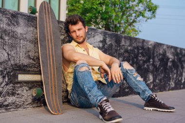 Sakallı, genç ve yakışıklı bir adam sokakta uzun tahtayla oturuyor..