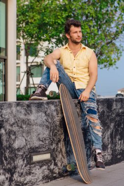 Sakallı, genç ve yakışıklı bir adam sokakta uzun tahtayla oturuyor..
