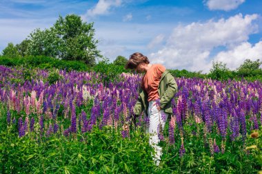 Yeşil ceketli uzun boylu yakışıklı bir adam lupin çiçeği tarlasında duruyor, doğanın güzelliğini emrediyor. Mor ve pembe lupinlerle çevrili bir adam..