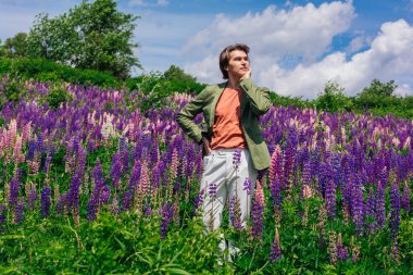 Yeşil ceketli uzun boylu yakışıklı bir adam lupin çiçeği tarlasında duruyor, doğanın güzelliğini emrediyor. Mor ve pembe lupinlerle çevrili bir adam..