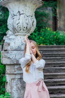 Dekoratif antika vazosu ve merdivenleri olan eski bir binanın yanında duran güzel sarışın bir kızın portresi.