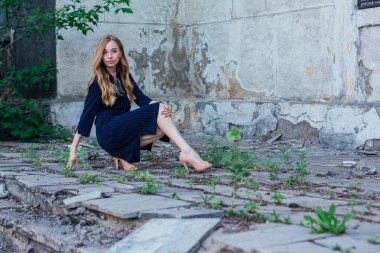 Gri duvarları olan eski bir binanın yanında oturan güzel sarışın kadın.