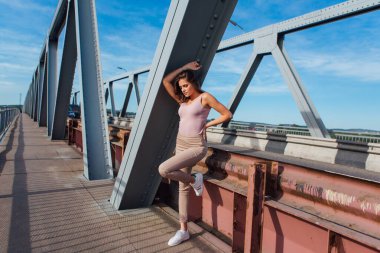 Gün batımında nehrin üzerindeki eski paslı nakliye köprüsünde poz veren genç ve güzel bir kadının ılık yaz portresi..