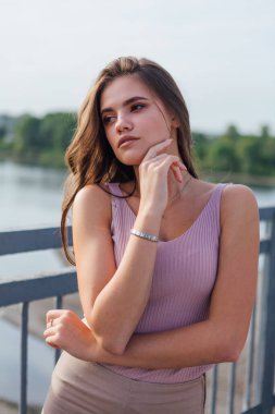 Gün batımında nehrin üzerindeki eski paslı nakliye köprüsünde poz veren genç ve güzel bir kadının ılık yaz portresini kapatın..