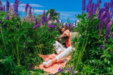 Yeşil ceketli uzun boylu yakışıklı bir adam lupin çiçeklerinin arasında oturmuş, doğanın güzelliğini emrediyor. Mor ve pembe lupinlerle çevrili bir adam..