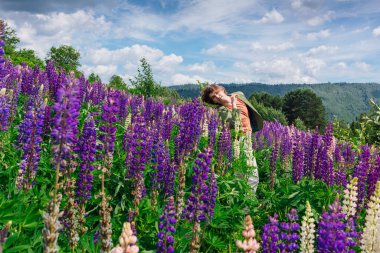Yeşil ceketli uzun boylu yakışıklı bir adam lupin çiçeği tarlasında duruyor, doğanın güzelliğini emrediyor. Mor ve pembe lupinlerle çevrili bir adam..