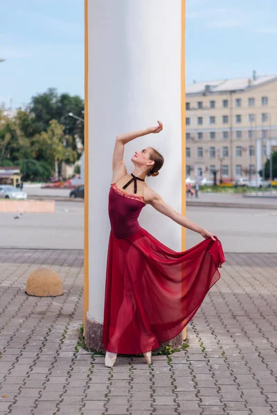 Woman ballerina in red ballet dress dancing in pointe shoes next to the old columns. Ballerina standing in beautiful ballet pose