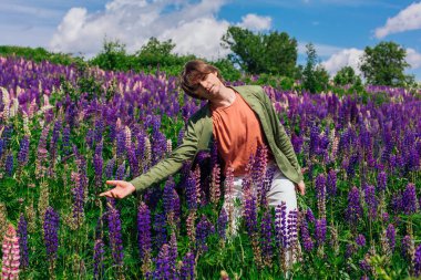 Yeşil ceketli uzun boylu yakışıklı bir adam lupin çiçeği tarlasında dans ediyor, doğanın güzelliğini emrediyor. Mor ve pembe lupinlerle çevrili bir adam..