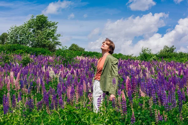 Yeşil ceketli uzun boylu yakışıklı bir adam lupin çiçeği tarlasında duruyor, doğanın güzelliğini emrediyor. Mor ve pembe lupinlerle çevrili bir adam..