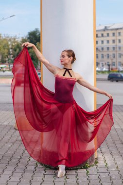 Kırmızı bale elbiseli kadın balerin eski sütunların yanında sivri ayakkabıyla dans ediyor. Balerin güzel bir bale pozisyonunda duruyor.