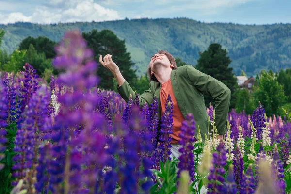 Yeşil ceketli uzun boylu yakışıklı bir adam lupin çiçeği tarlasında duruyor, doğanın güzelliğini emrediyor. Mor ve pembe lupinlerle çevrili bir adam..