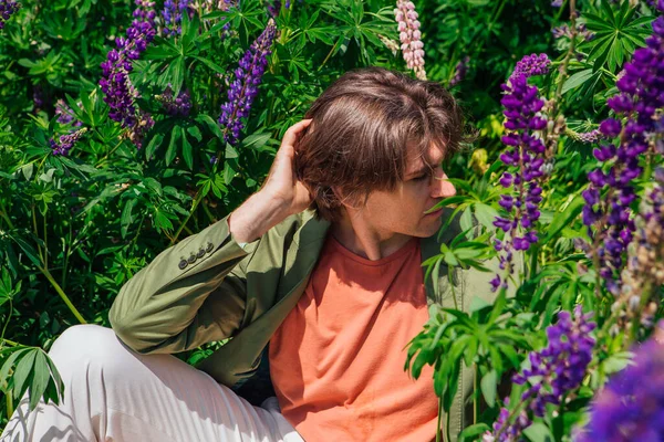 Yeşil ceketli uzun boylu yakışıklı bir adam lupin çiçeklerinin arasında oturmuş, doğanın güzelliğini emrediyor. Mor ve pembe lupinlerle çevrili bir adam..