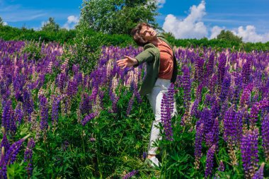 Yeşil ceketli uzun boylu yakışıklı bir adam lupin çiçeği tarlasında dans ediyor, doğanın güzelliğini emrediyor. Mor ve pembe lupinlerle çevrili bir adam..
