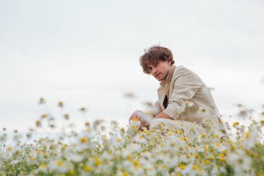 Beyaz takım elbiseli uzun boylu, yakışıklı bir adam papatya çiçekleri tarlasında bir sandalyenin arkasında oturuyordu.