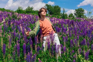 Uzun boylu, yakışıklı bir adam Lupin çiçeklerinin arasında dans ediyor.