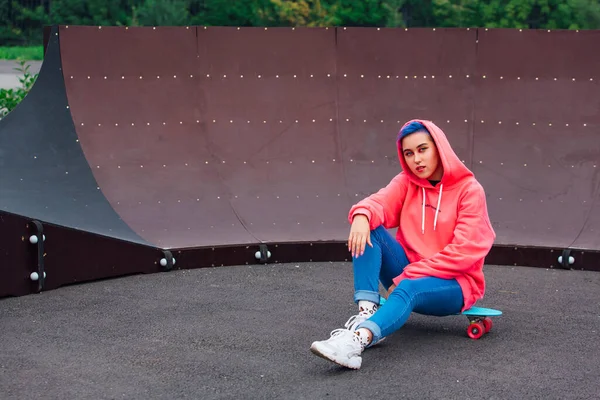 Stijlvolle jonge vrouw zittend op haar plastic skateboard in skatepark. Jeugdconcept. — Stockfoto