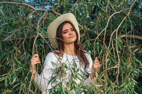 Jong mooi brunette vrouw staan dicht bij de boom brunches met groene bladeren — Stockfoto