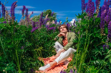 Lupin çiçeklerinin arasında oturan uzun boylu yakışıklı adam.