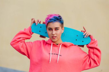 Omuzlarında mavi plastik kaykay tutan kısa saçlı şık genç bir kadın. Gençlik kavramı.