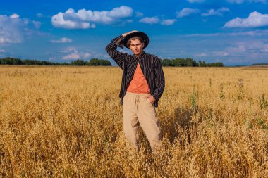 Kırsal Kır Sahnesi. Siyah gömlekli ve siyah şapkalı uzun boylu yakışıklı adam altın yulaf tarlasında duruyordu. Mavi gökyüzü ile yaz manzarası