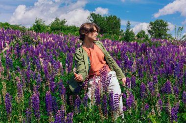 Yeşil ceketli uzun boylu yakışıklı bir adam lupin çiçeği tarlasında dans ediyor, doğanın güzelliğini emrediyor. Mor ve pembe lupinlerle çevrili bir adam..