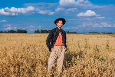 Kırsal Kır Sahnesi. Siyah gömlekli ve siyah şapkalı uzun boylu yakışıklı adam altın yulaf tarlasında duruyordu. Mavi gökyüzü ile yaz manzarası